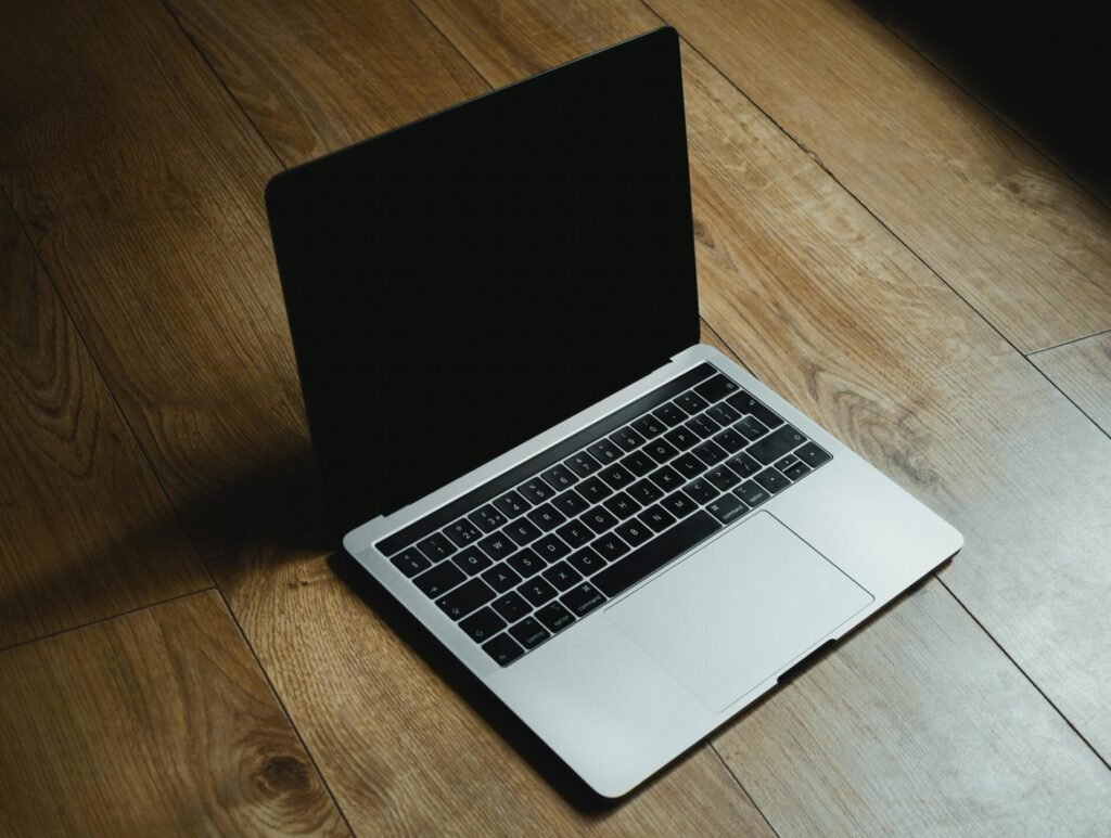 MacBook placed diagonally on a warm wooden floor with soft lighting.