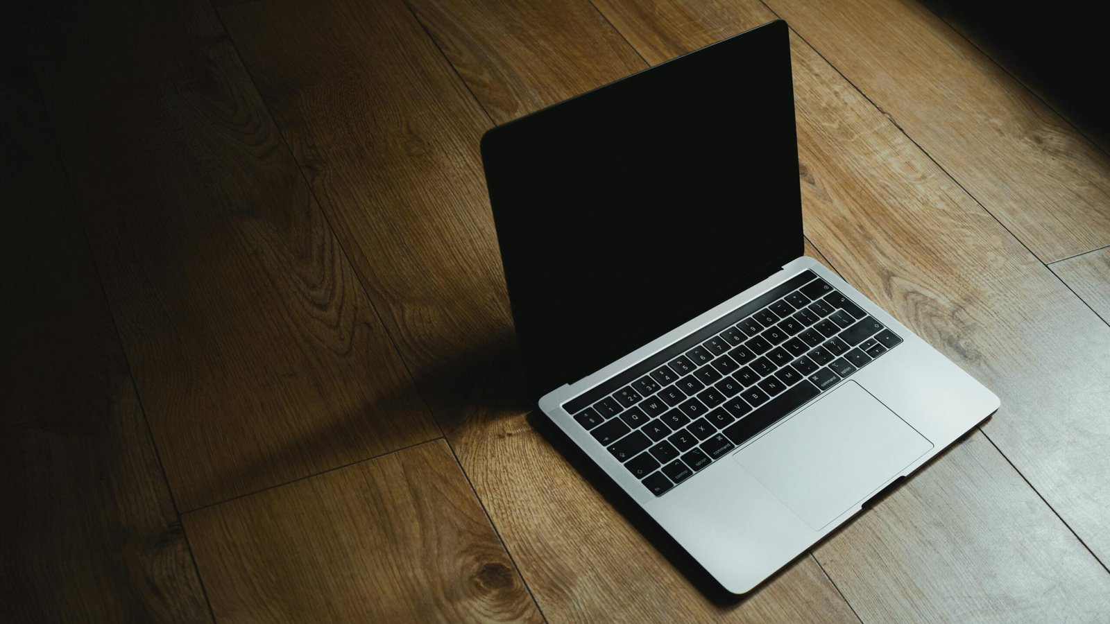 MacBook placed diagonally on a warm wooden floor with soft lighting.